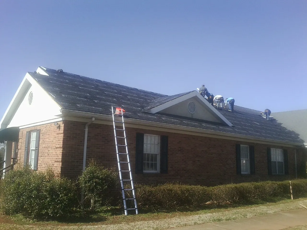 Crew tearing shingles off a brick ranch roof with a ladder set — Emergency Roof Repair work by our crew in La Marque