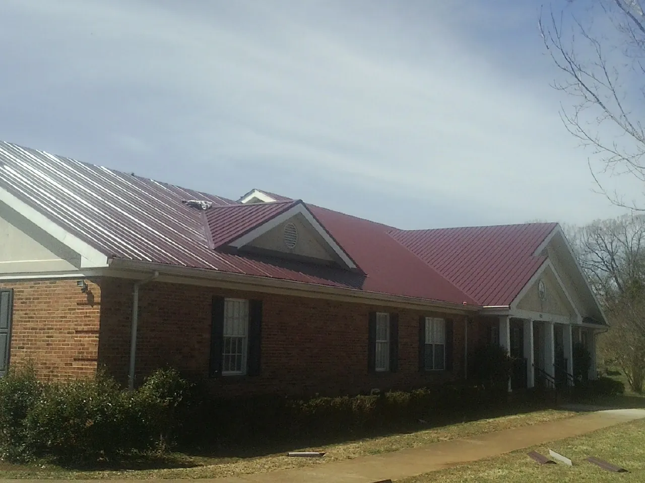 Red metal roof with gabled entries on a long brick building, from a Hail Damage Roof Repair job in La Marque