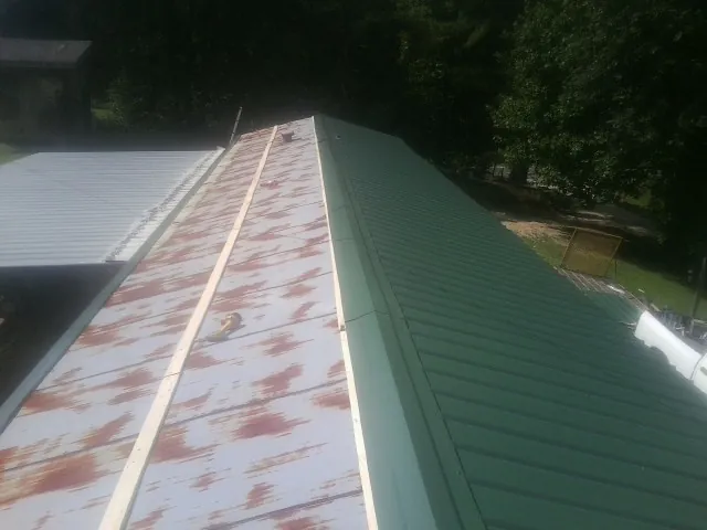 Old rusted panels beside newly installed green metal roofing — Wind Damage Roof Repair by Roofing Brothers in La Marque