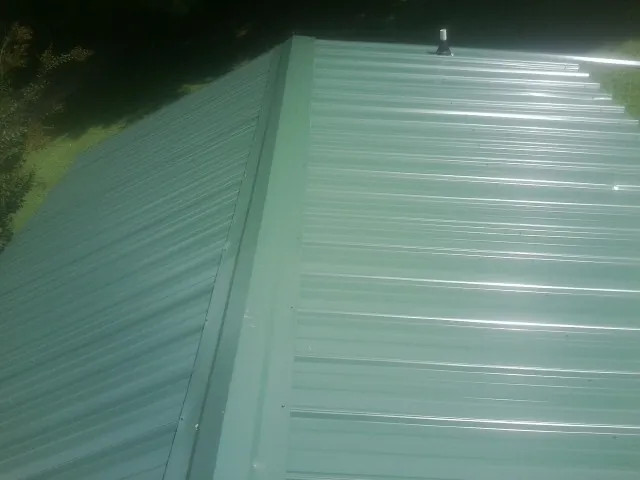 New green metal panels meeting at the ridge of a roof — Flat Roof Repair work by our crew in La Marque