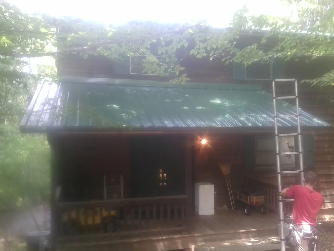Worker on a ladder at the green porch roof of a wooded cabin in La Marque